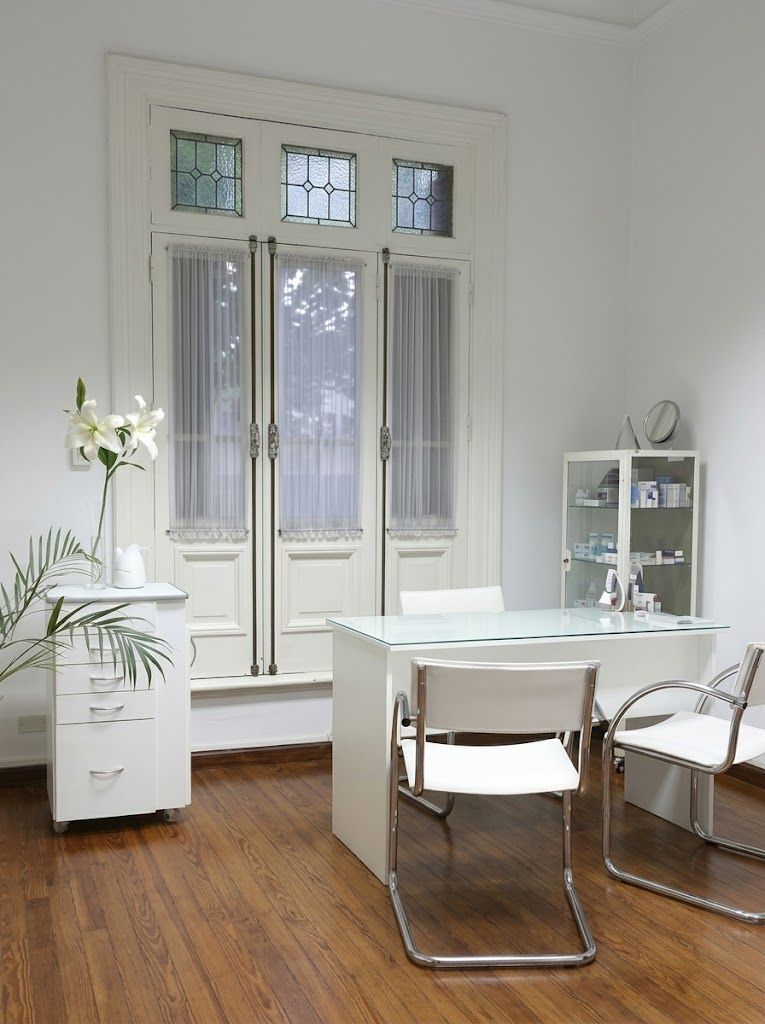 Consultorio con escritorio, sillas blancas y puertas altas con vitraux